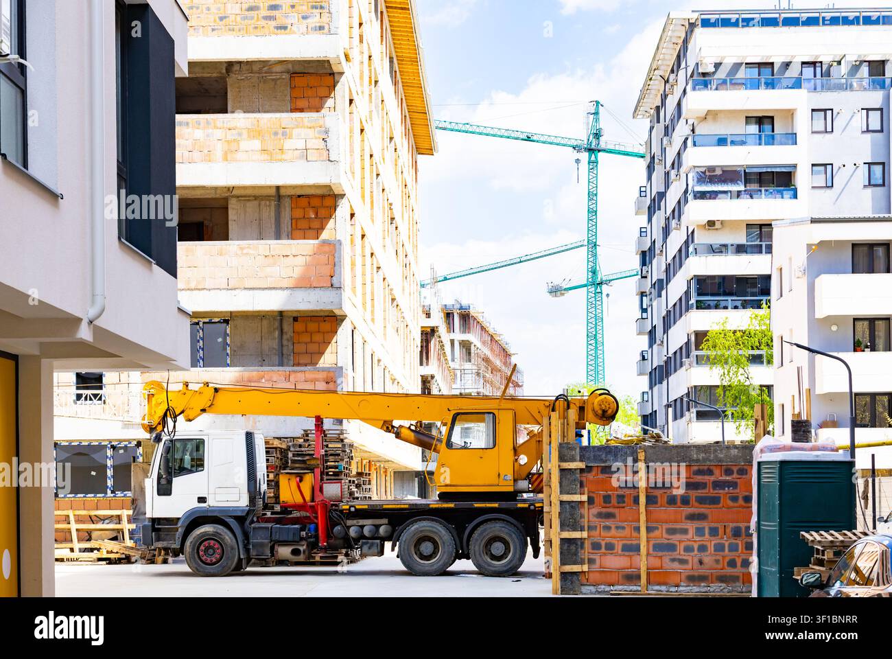 Gru mobile gialla parcheggiata in un cantiere edile urbano di un edificio residenziale con gru torre alte sullo sfondo Foto Stock