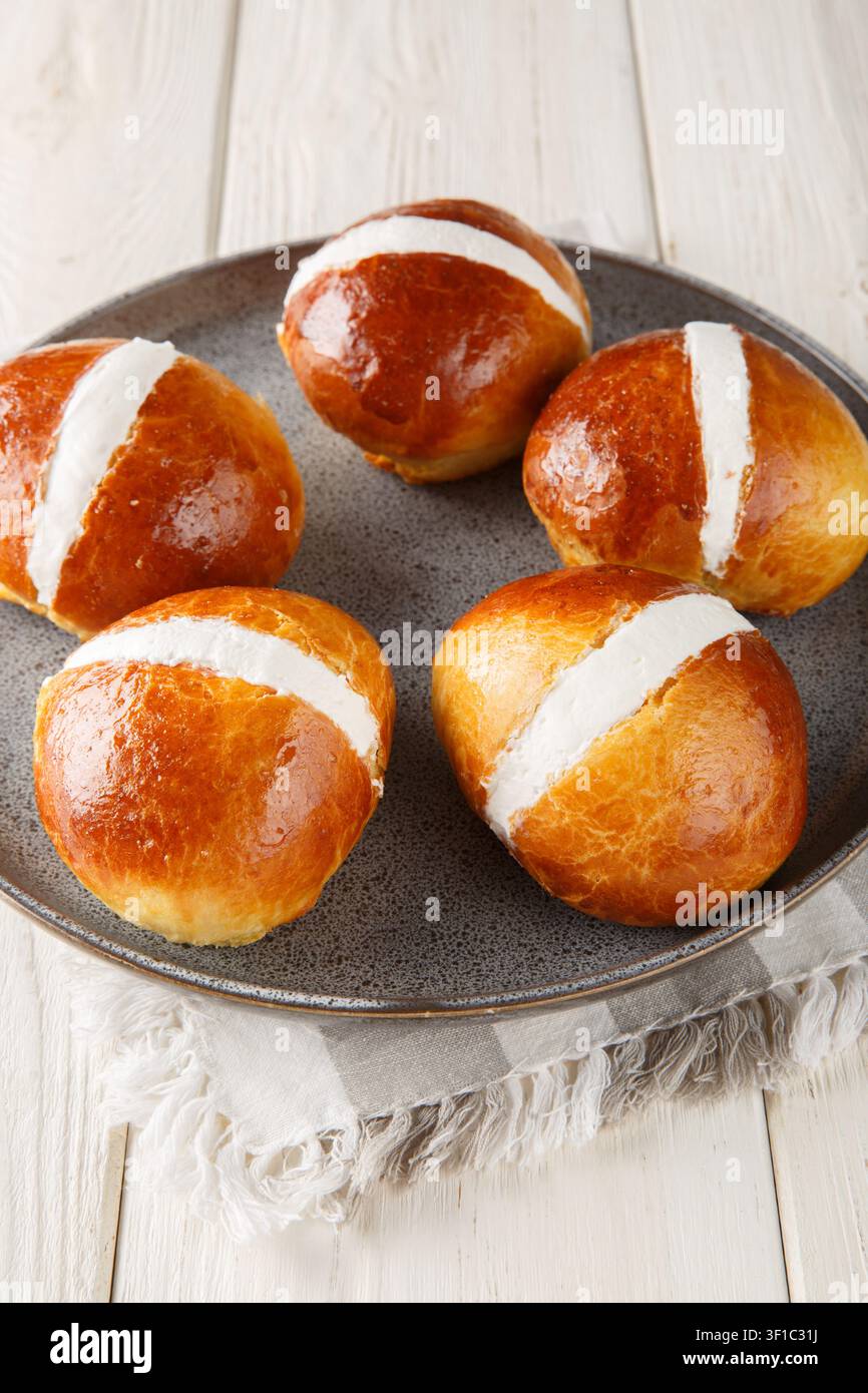 i deliziosi Maritozzi romani sono panini incredibilmente leggeri, morbidi e dolci, ripieni di abbondante panna montata perfetta, primo piano in un piatto sul tavolo. Verticale Foto Stock