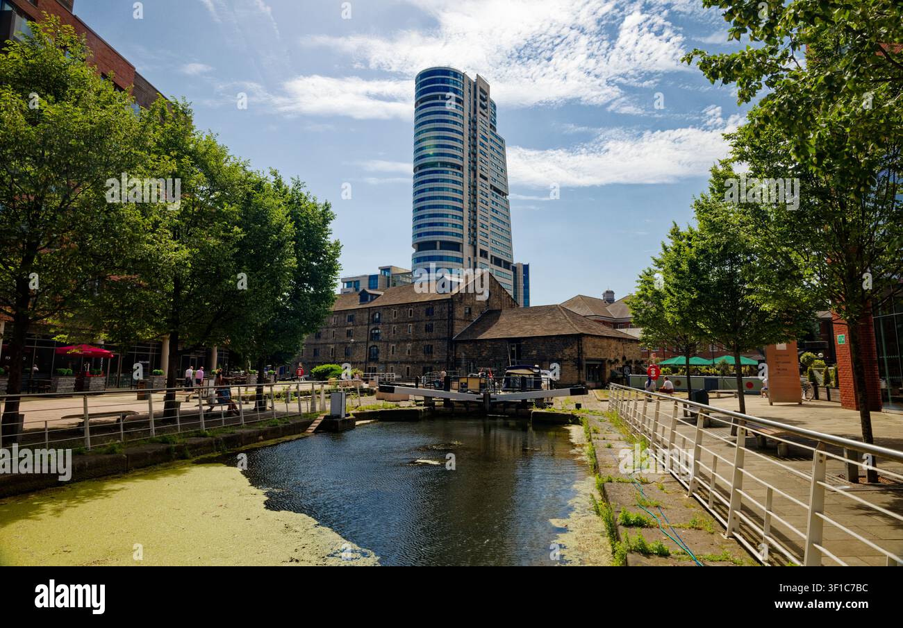 Un grattacielo alto si erge su un molo di canale rigenerato con bar, una chiuse e alberi, Granary Wharf, Leeds, West Yorkshire, Inghilterra. Foto Stock