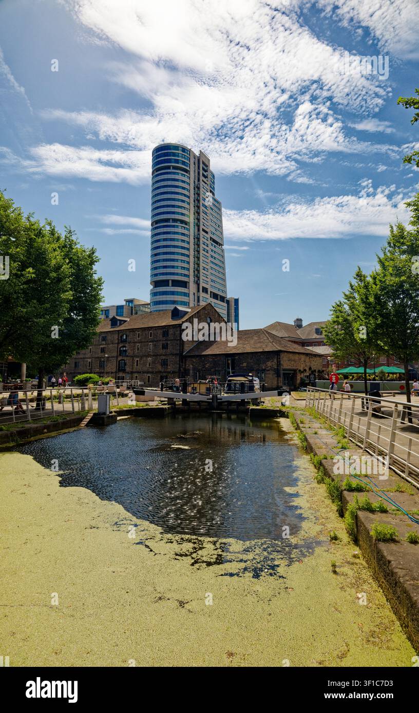 Un grattacielo alto si erge su un molo di canale rigenerato con bar, una chiuse e alberi, Granary Wharf, Leeds, West Yorkshire, Inghilterra. Foto Stock