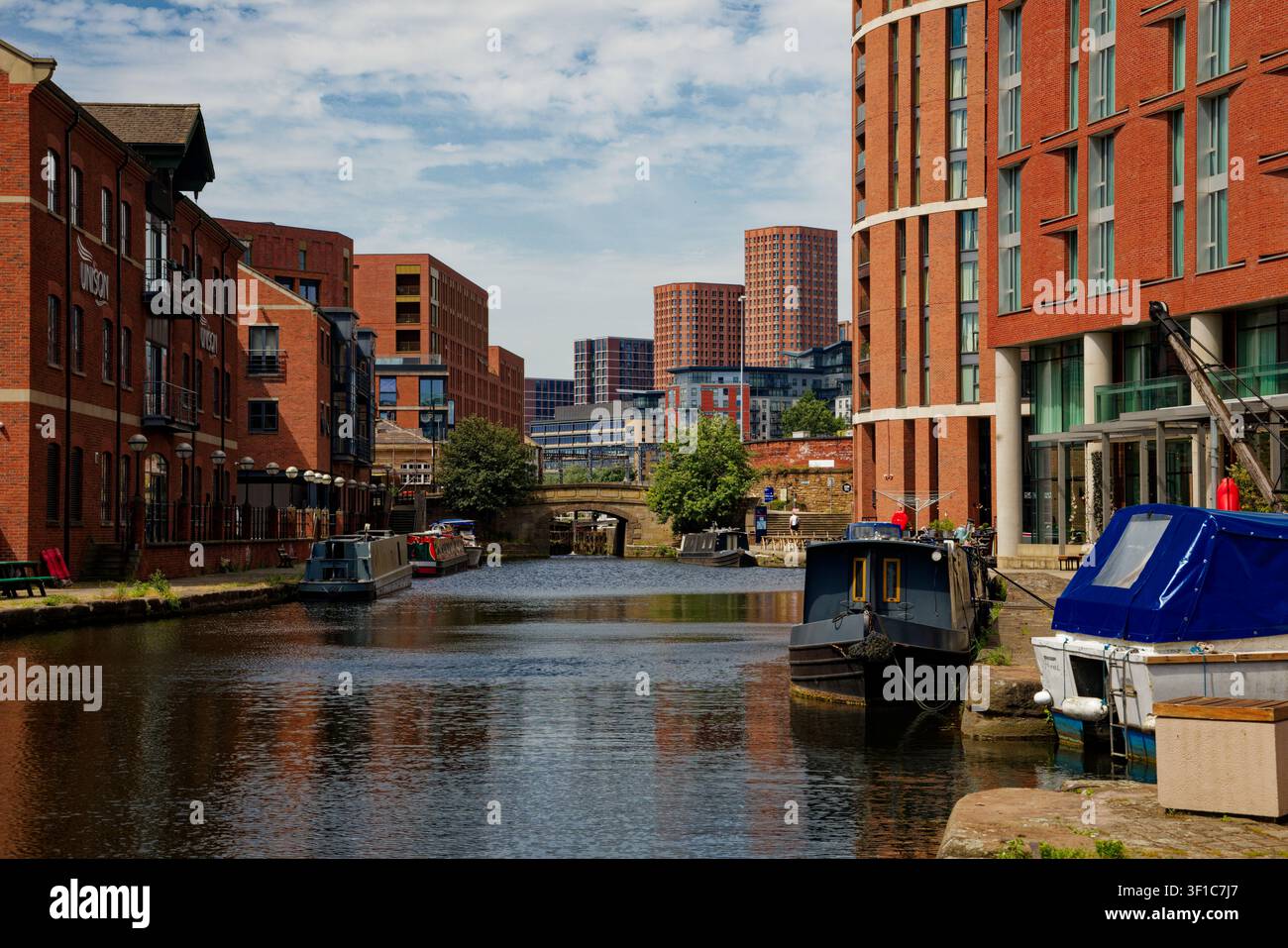 Un tratto di canale urbano con chiatte ormeggiate ai lati e alti condomini in lontananza, Leeds, West Yorkshire, Inghilterra. Foto Stock