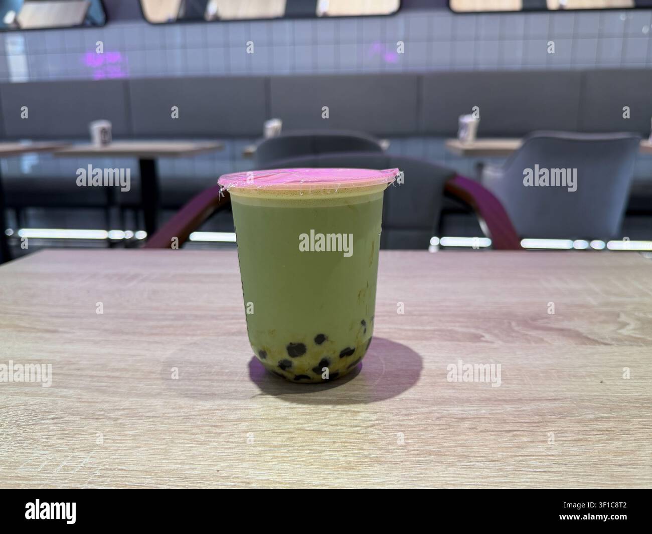 Tè alle bolle al matcha con perle di tapioca in una tazza da asporto posizionata su un tavolo di legno del caffè, con spazio per il testo. Cultura del caffè, tendenza alimentare, stile di vita, rinfresco Foto Stock