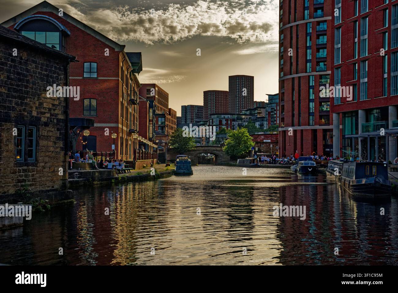 La luce della sera svanisce oscurando il cielo sopra una scena di canale urbano con uffici, appartamenti e persone nei bar, Granary Wharf, Leeds, West Yorkshire. Foto Stock