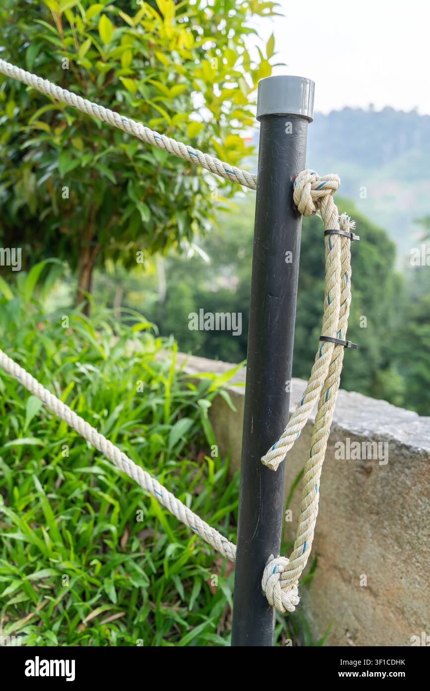 Un primo piano di un palo in metallo nero con ringhiere spesse in corda lungo un sentiero del giardino panoramico e circondato da una vegetazione rigogliosa Foto Stock