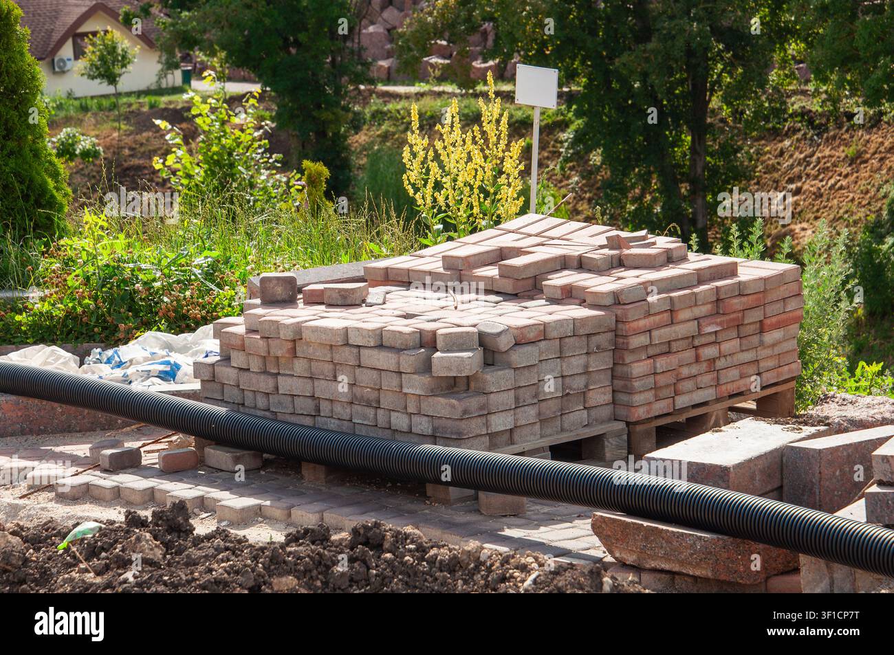 Una grande pila di pietre da pavimentazione rettangolari è posata su bancali di legno, in attesa di installazione per un sentiero da giardino o una costruzione di patio Foto Stock