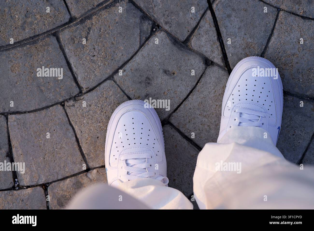 Persona con scarpe da ginnastica bianche moderne che esplora un ambiente urbano all'aperto, in piedi su una strada lastricata grigia texturizzata, evidenziando il contemporaneo Foto Stock