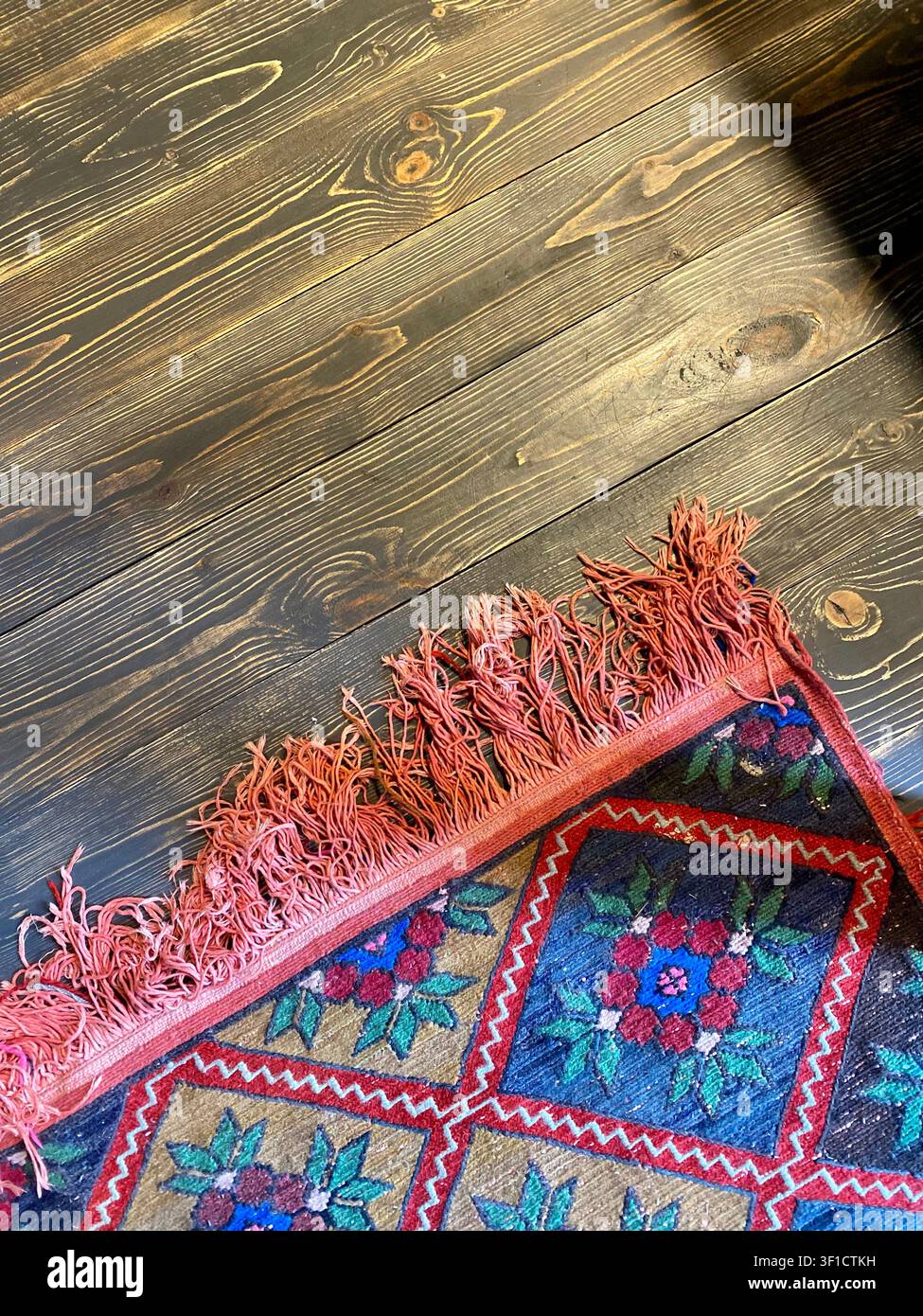 Tappeto tessuto tradizionale su pavimento di legno scuro con texture rustica e motivo etnico. - Immagine stock catturata con smartphone