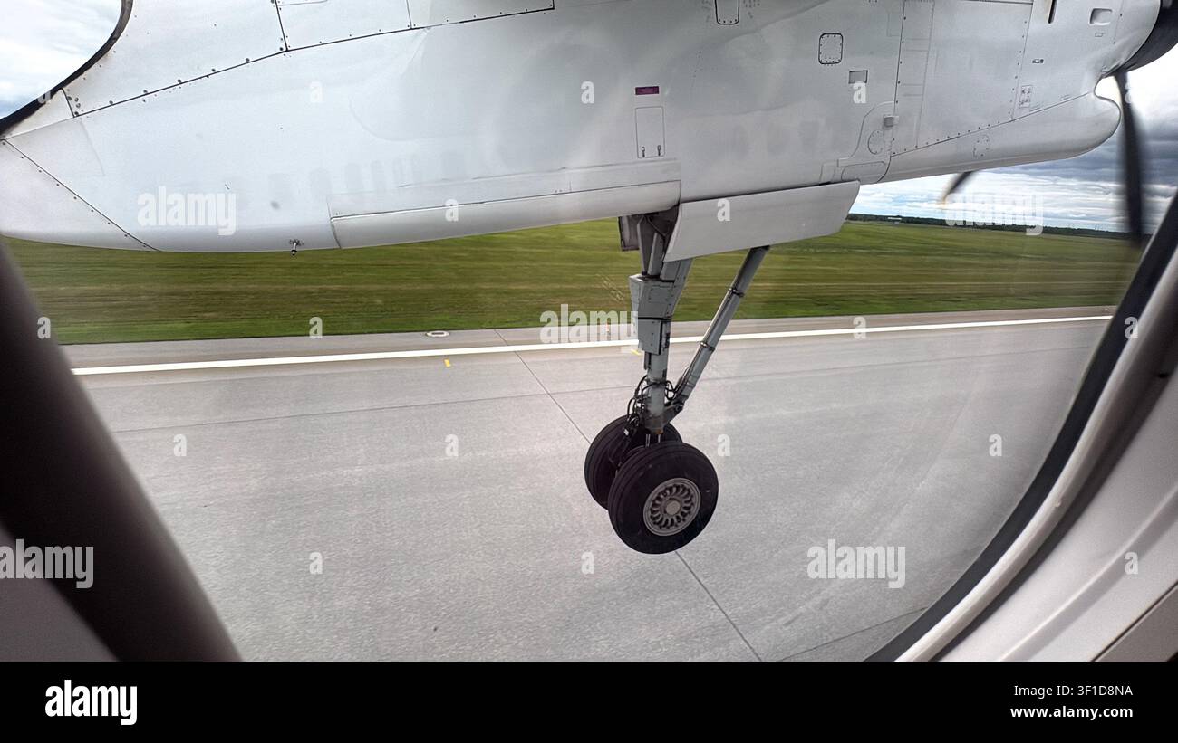 Treno di atterraggio con pneumatici doppi visto attraverso il finestrino di un aereo regionale turboelica mentre l'aereo decolla dall'aeroporto. Foto Stock