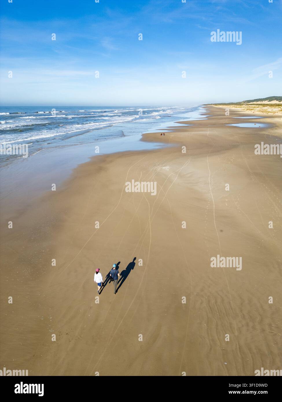 Una coppia in abiti da trekking cammina lungo la spiaggia a Torres, Rio Grande do Sul, Brasile, con una vasta veduta della costa che si estende nella Foto Stock