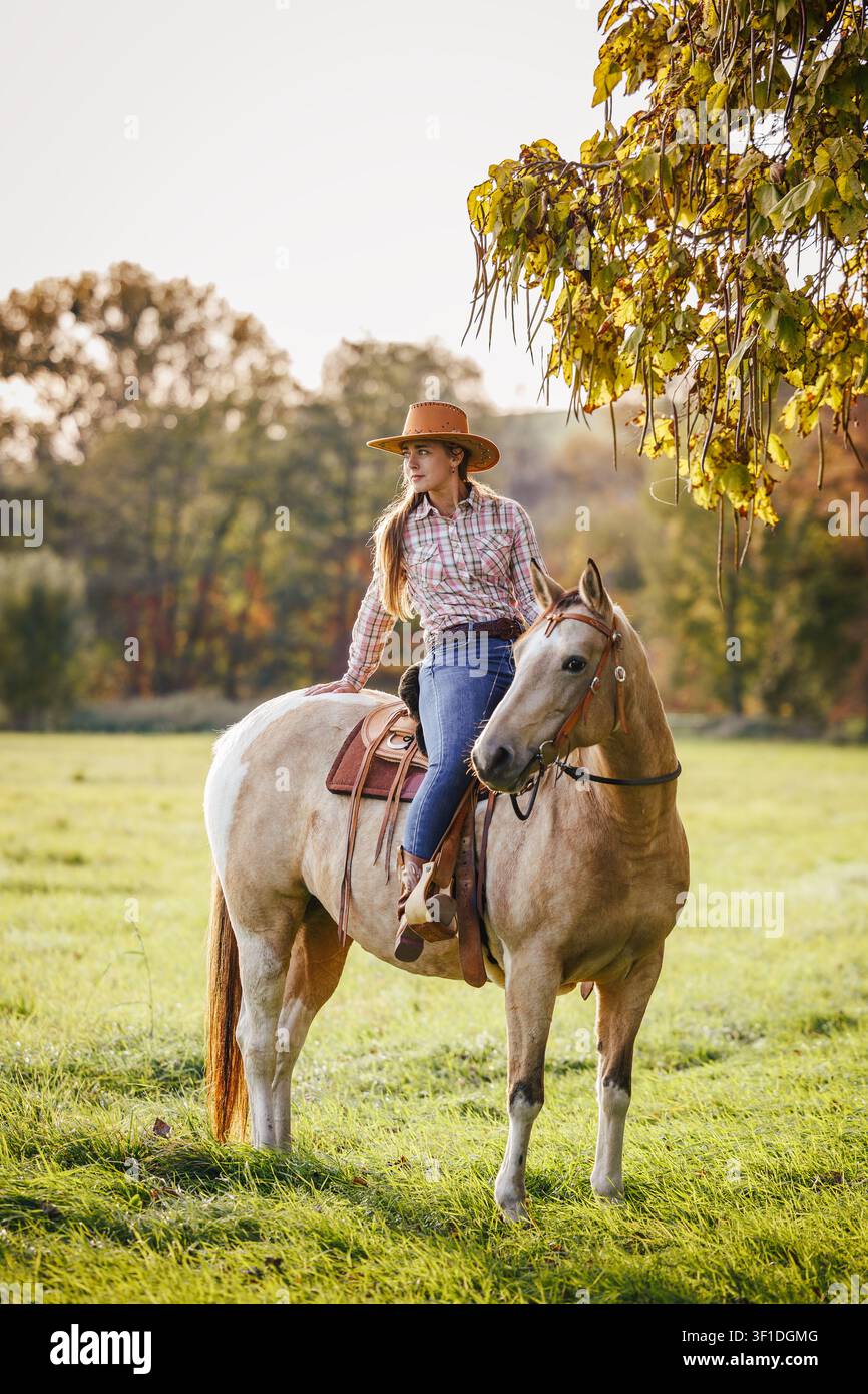 Cavallerizza che riposa sul cavallo in un paesaggio rurale autunnale. Cowgirl che cavalca in stile western Foto Stock