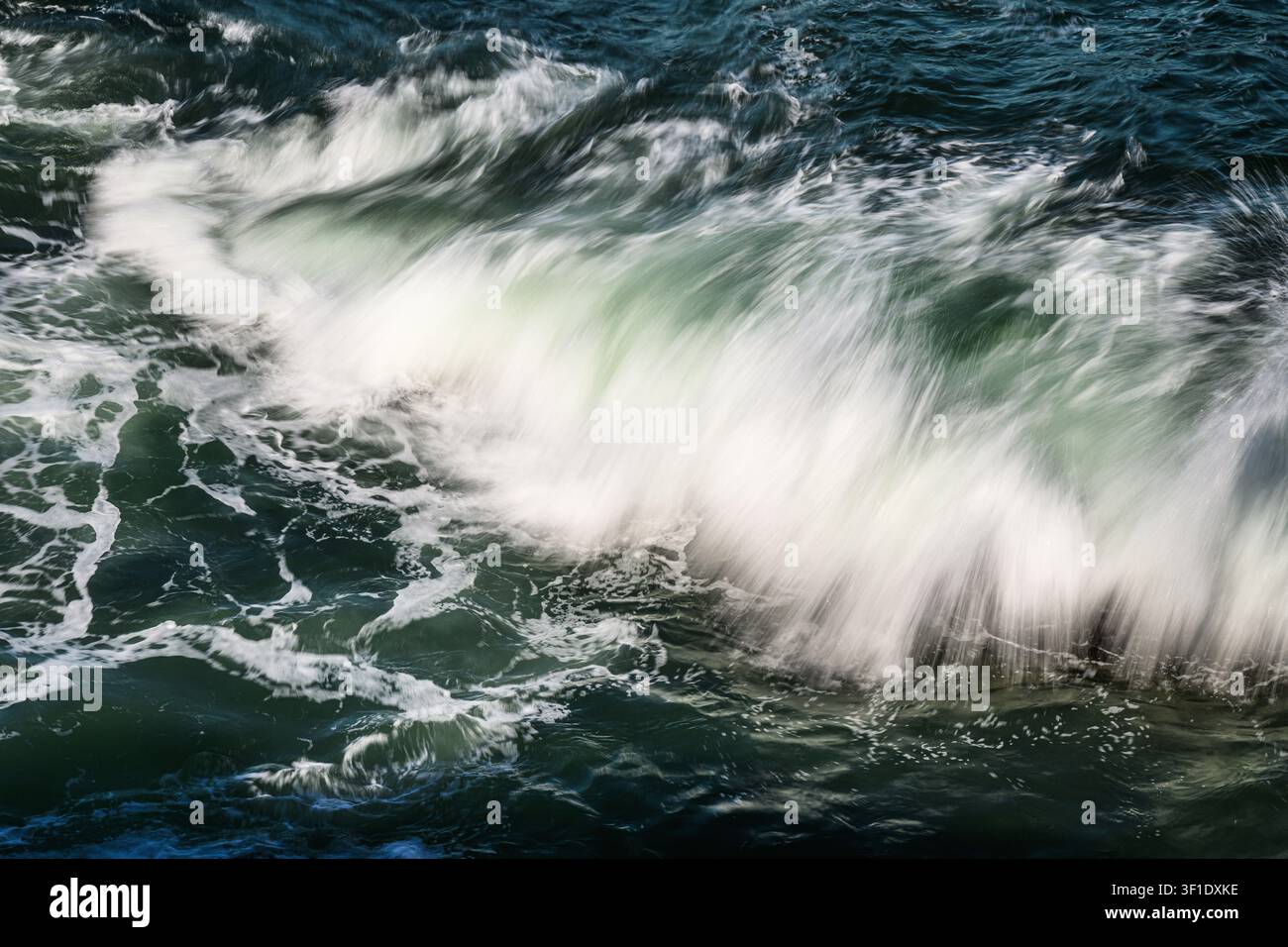 Dettaglio ravvicinato di un'onda oceanica che si infrange in movimento schizzante, dando un bordo anteriore piumato all'onda in arrivo Foto Stock