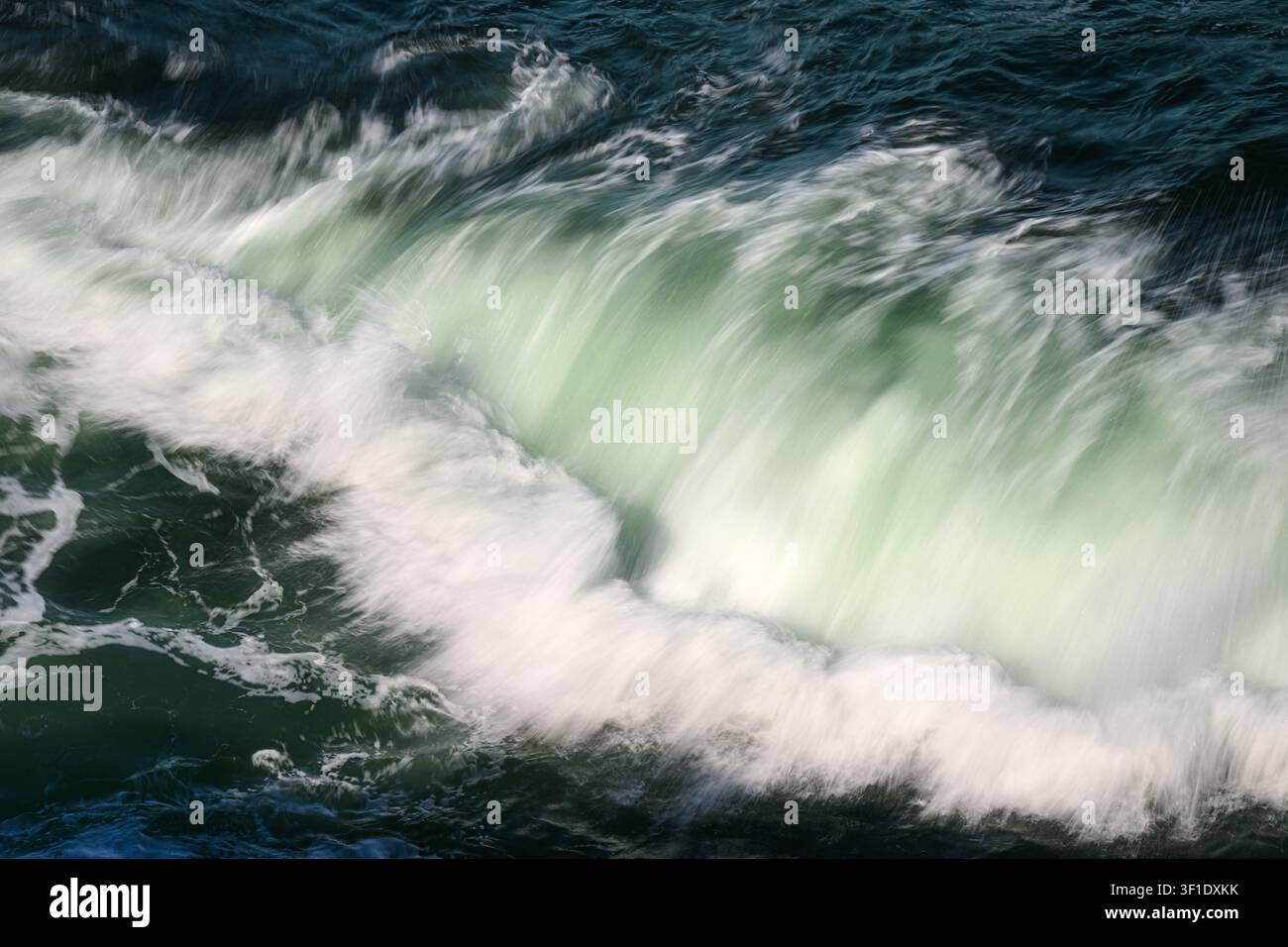 Dettaglio ravvicinato mentre un'onda dell'oceano si infrange creando un bordo schiumoso bianco con colore verde nell'onda Foto Stock