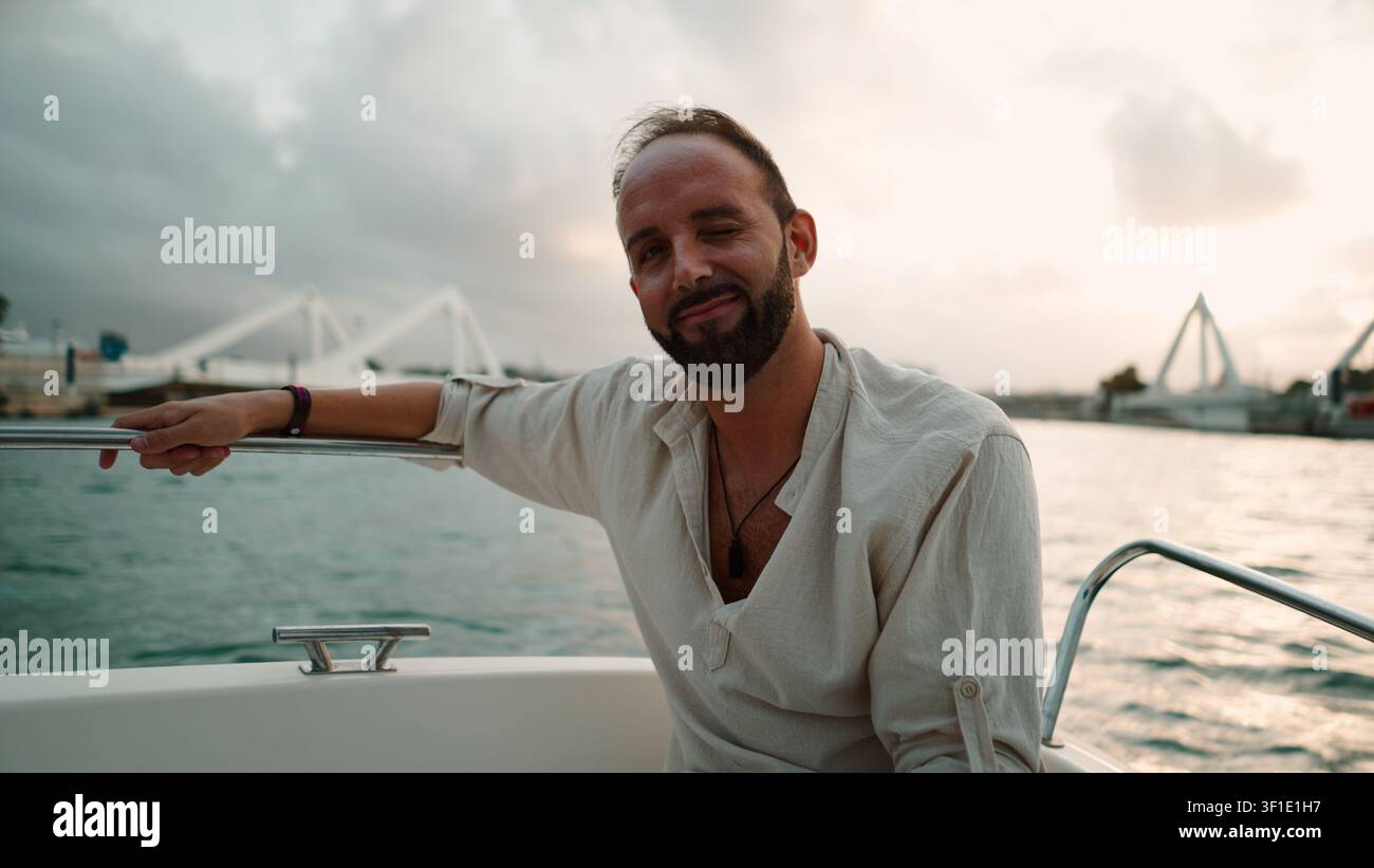 Giovane uomo che sorride e ammicca durante un'escursione in barca al tramonto Foto Stock