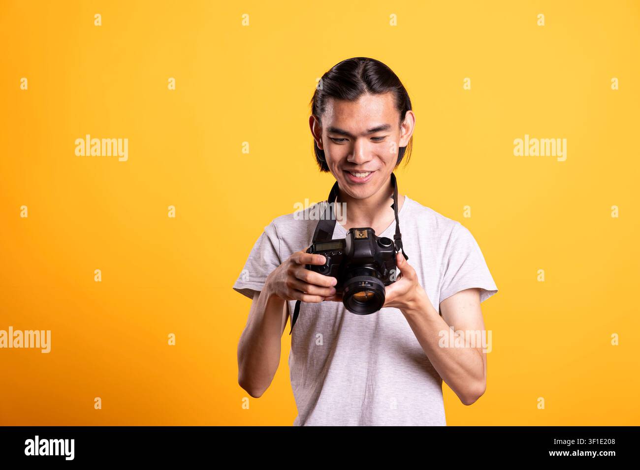 Fotografo maschio gioioso che tiene una fotocamera DSLR e rivede le foto sullo schermo dopo lo scatto. Cameraman entusiasta che controlla le immagini catturate, soddisfatto dei risultati durante una sessione professionale in studio. Foto Stock