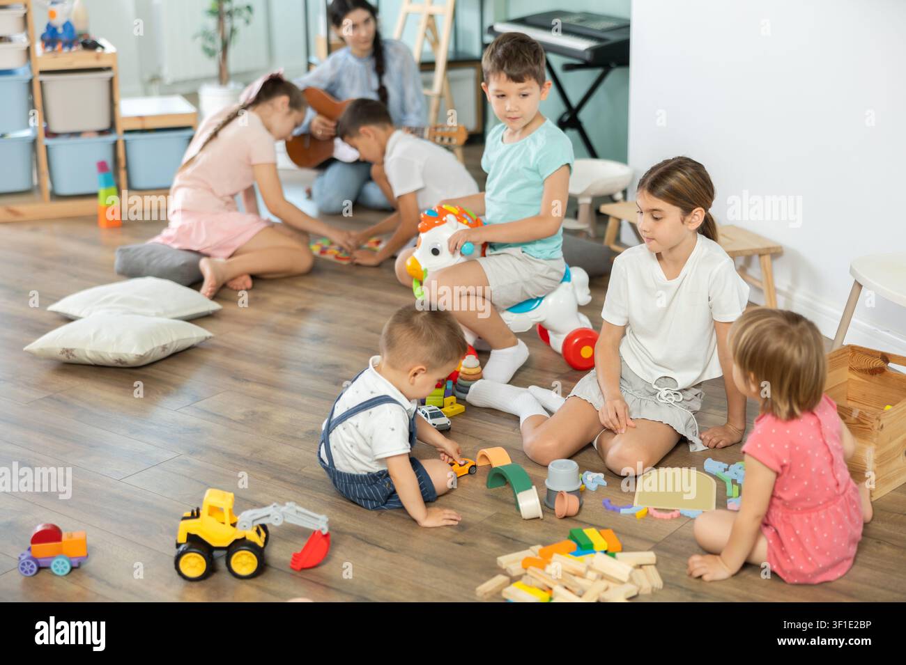 Bambini che giocano con giocattoli seduti sul pavimento nell'asilo Foto Stock