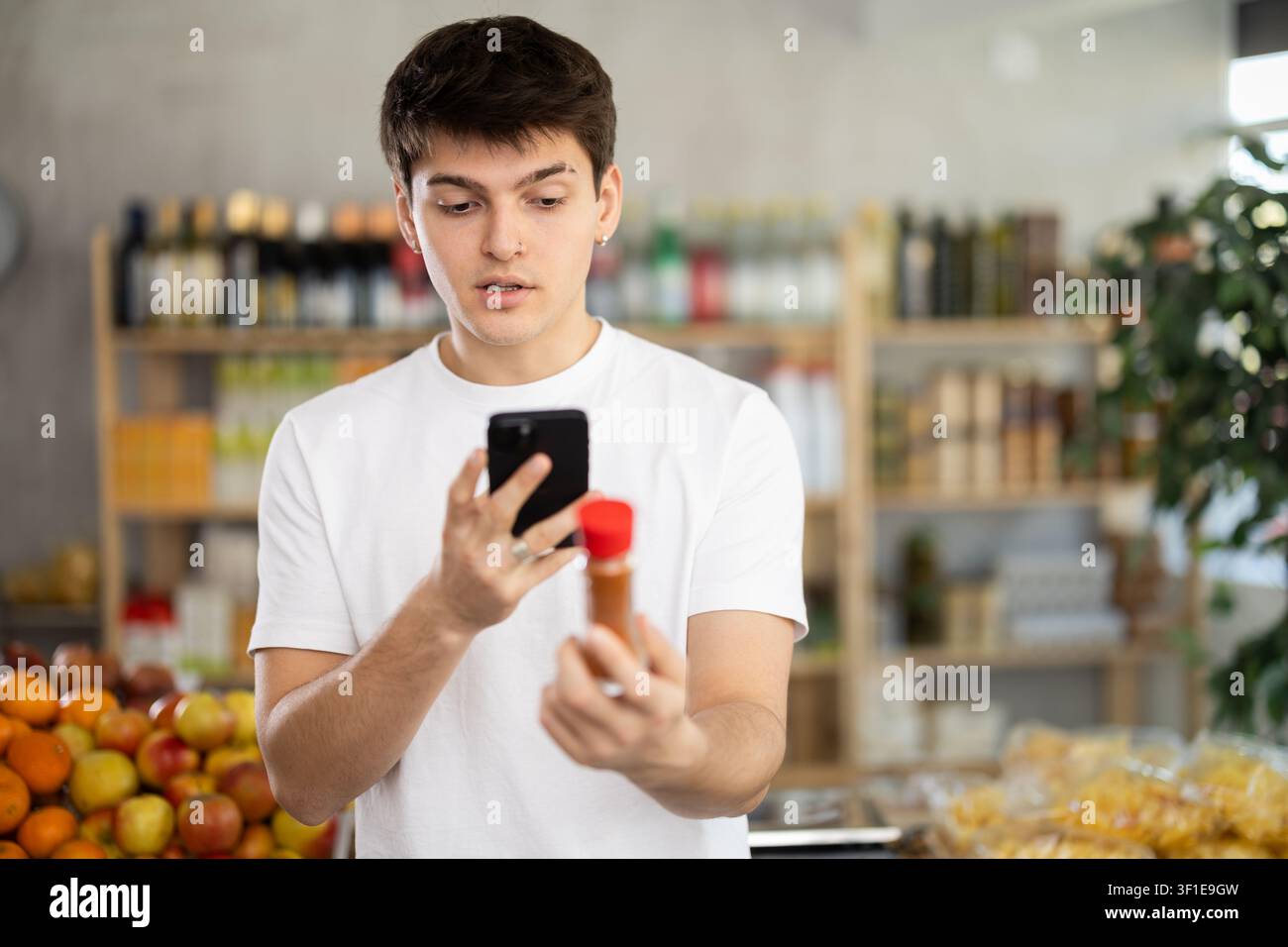 Ragazzo che scansiona il codice QR sull'etichetta del cardamomo in bottiglia nel reparto di alimentari del supermercato Foto Stock