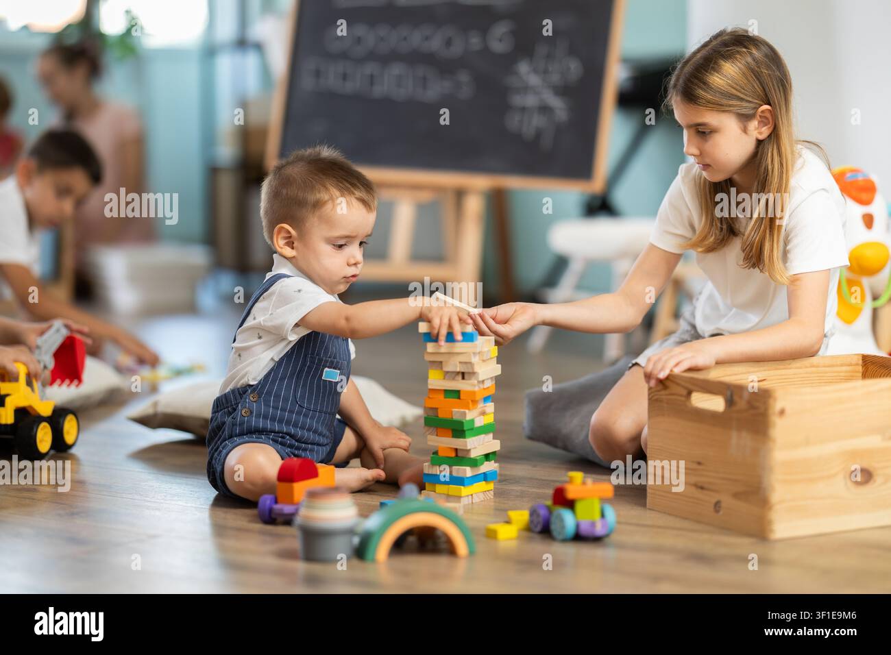Bambini che giocano con giocattoli seduti sul pavimento nell'asilo Foto Stock