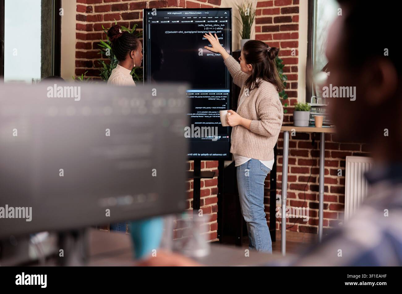 Team di programmazione discute algoritmi davanti a un grande schermo, analizzando script HTML, lavoro su database e programmazione della finestra del terminale. Foto Stock