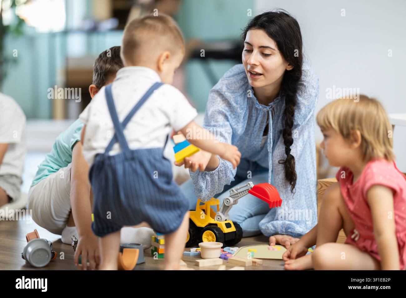Bambini che giocano con giocattoli con l'insegnante nelle vicinanze all'asilo Foto Stock