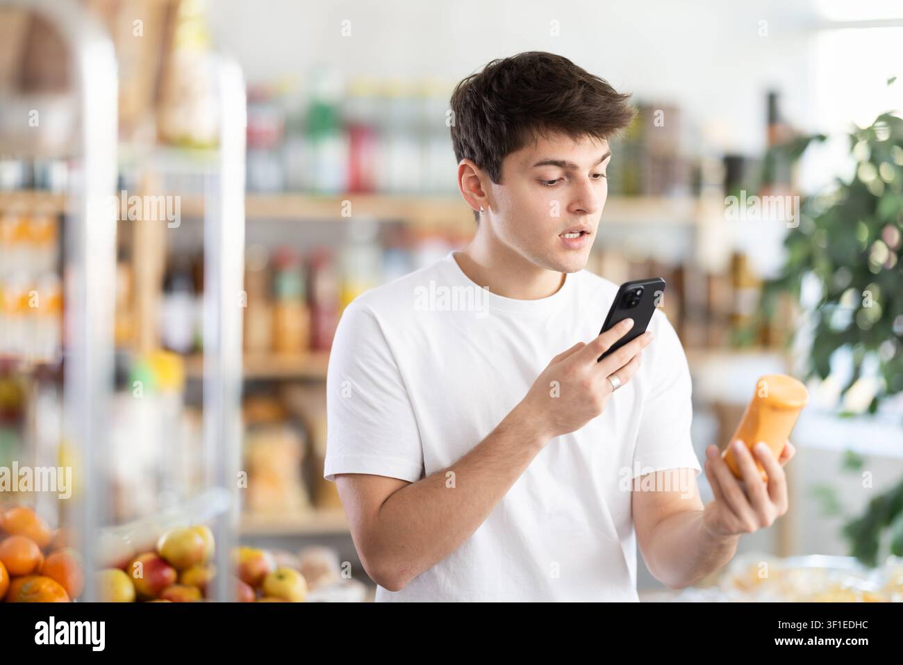 Acquirente maschio controlla l'idoneità - scansiona il codice QR sull'etichetta di un barattolo di salsa piccante nel negozio di alimentari Foto Stock