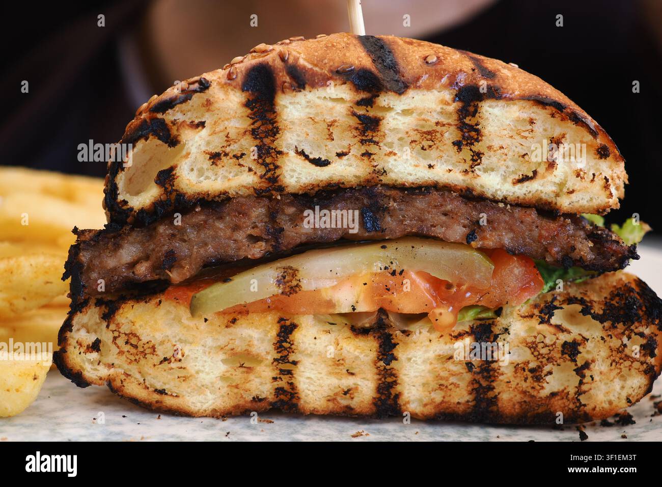 Hamburger succoso con panino grigliato e patatine fritte su un piatto Foto Stock
