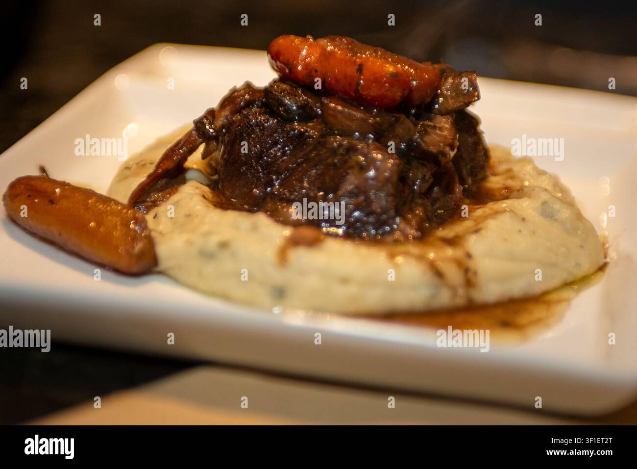 Una fotografia in stile ristorante in primo piano di costine di manzo saporite brasate o arrosto, ricoperte di carotine glassate e sugo ricco, appoggiate su un Be Foto Stock
