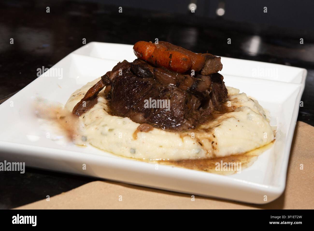 Una fotografia in stile ristorante in primo piano di costine di manzo saporite brasate o arrosto, ricoperte di carotine glassate e sugo ricco, appoggiate su un Be Foto Stock