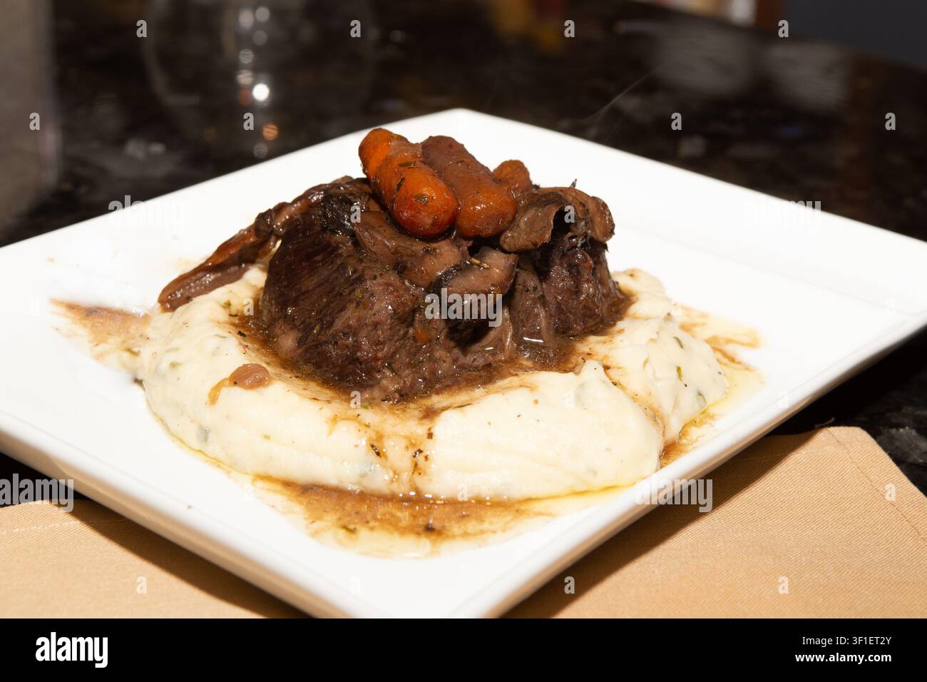 Una fotografia in stile ristorante in primo piano di costine di manzo saporite brasate o arrosto, ricoperte di carotine glassate e sugo ricco, appoggiate su un Be Foto Stock