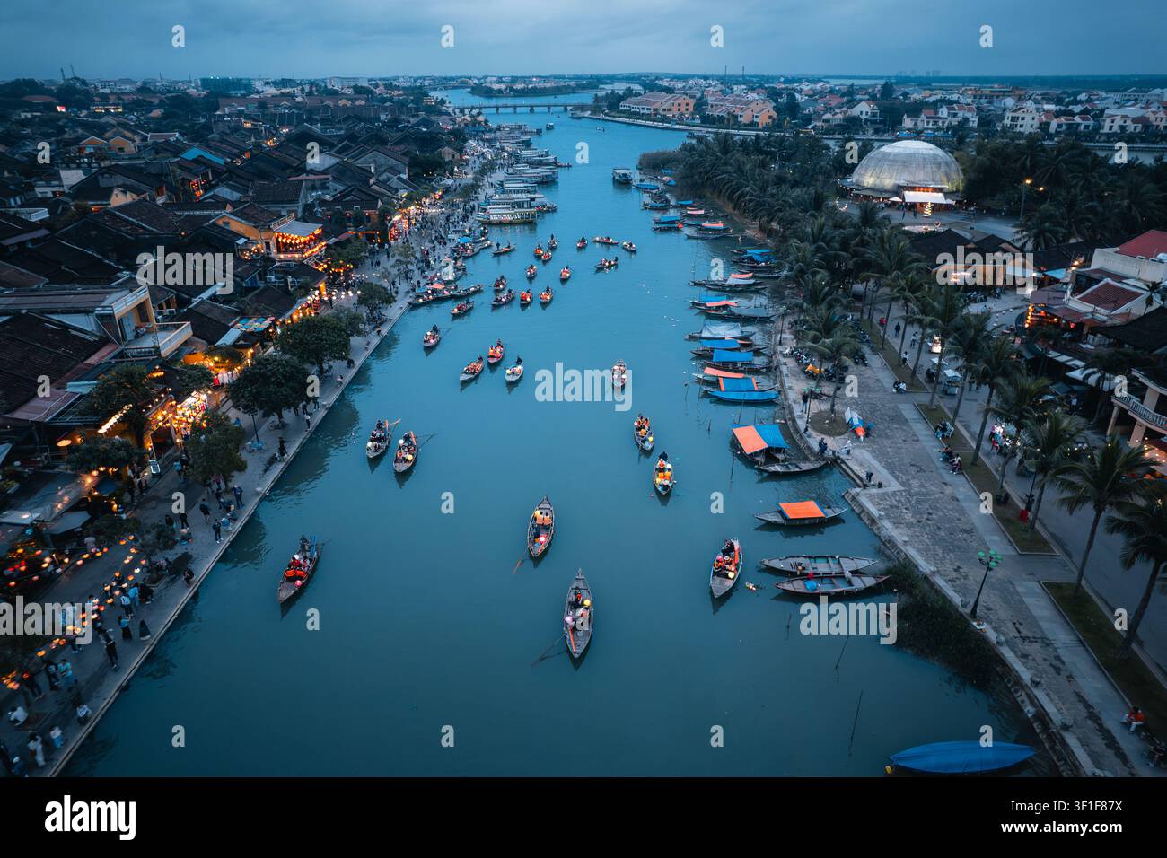 Vista aerea di Lantern Riverside Hoi An con tradizionali barche di legno che galleggiano sul fiume, illuminate da lanterne luminose lungo la città storica b Foto Stock
