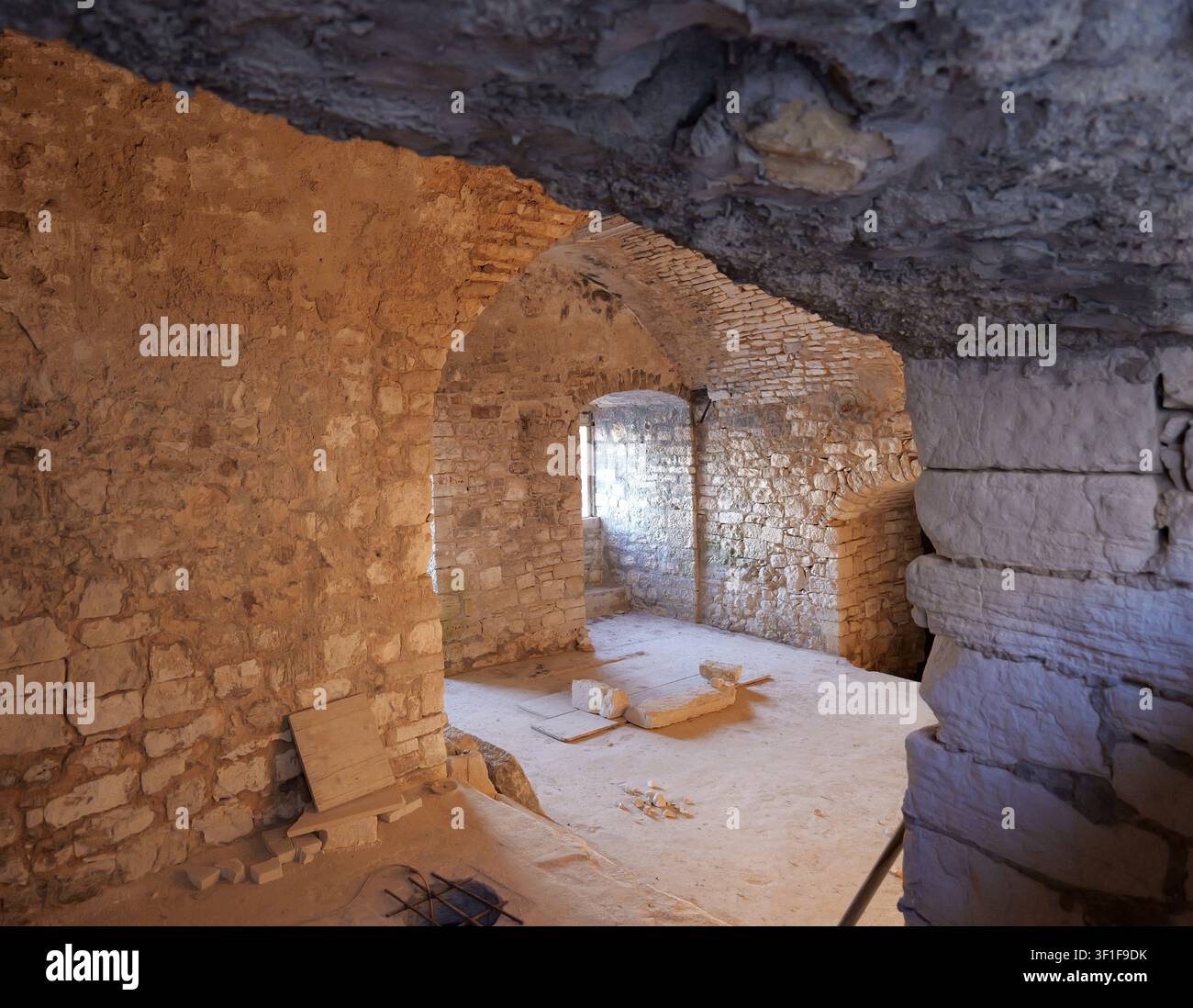 Mura e pavimento in pietra che formano una cella di prigione antica o una stanza del seminterrato. La luce entra da una piccola finestra alta. Italia, Giovinazzo, 19 luglio 2025 Foto Stock