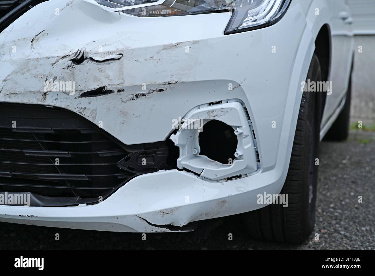 Paraurti anteriore danneggiato di un'auto bianca dopo un incidente stradale, vista ravvicinata con graffi. Foto Stock