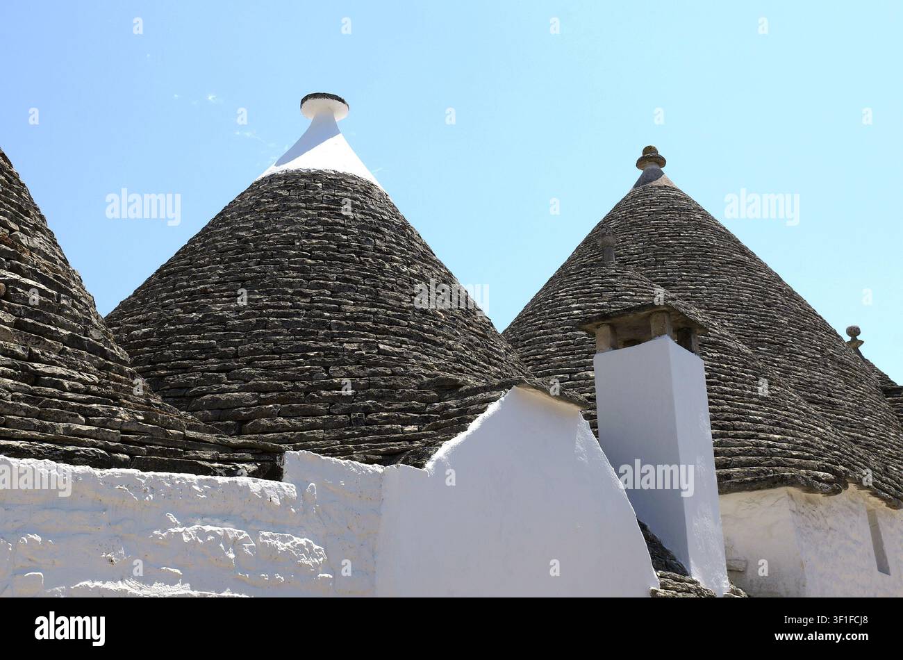 Architettura Trulli che forma una scena di villaggio tradizionale italiano. Muri imbiancati a contrasto con tetti conici in pietra secca grigia. Italia, Puglia, Albe Foto Stock