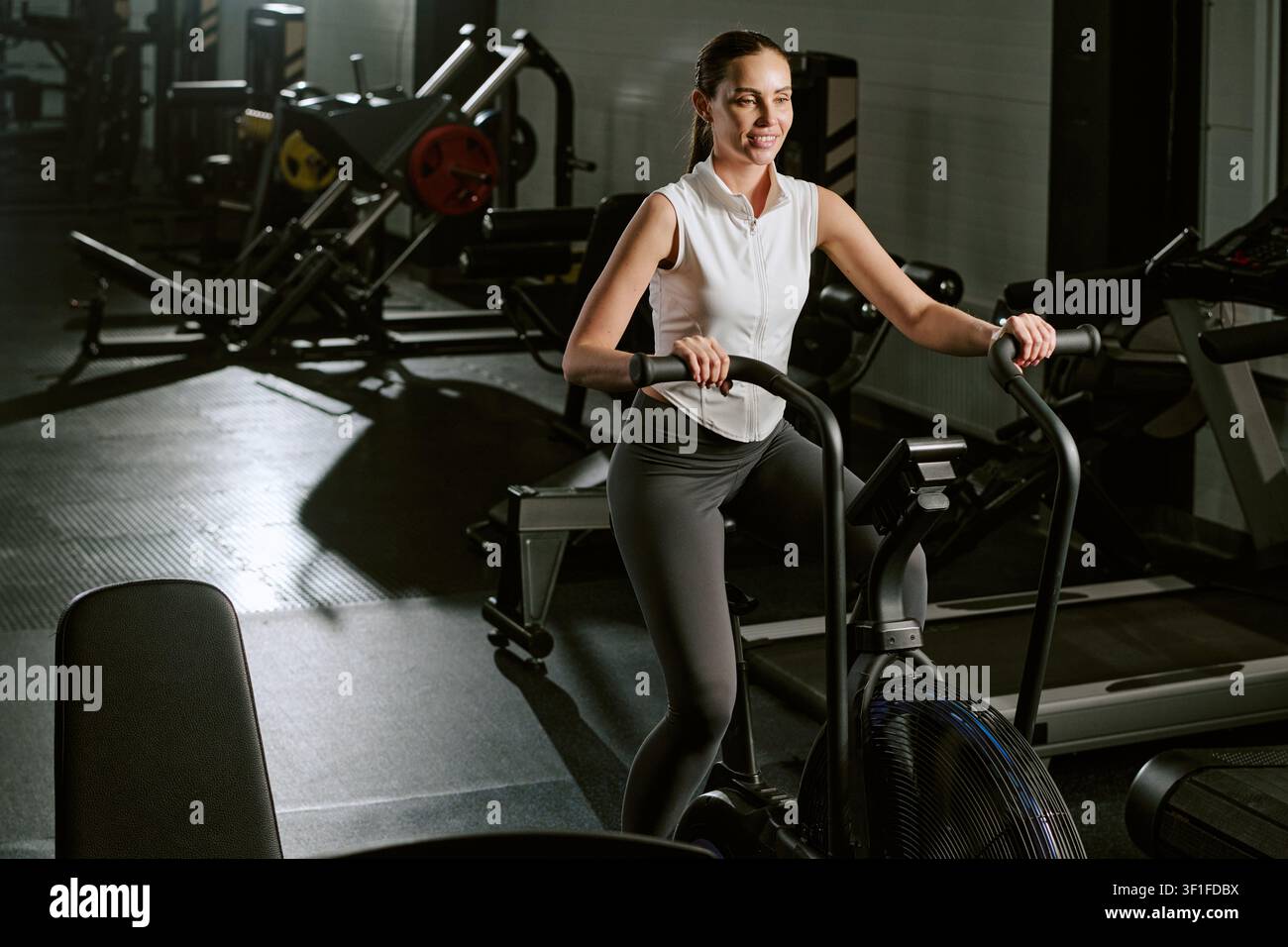 Giovane donna che fa esercizio su bicicletta aerobica per l'allenamento fisico in palestra Foto Stock