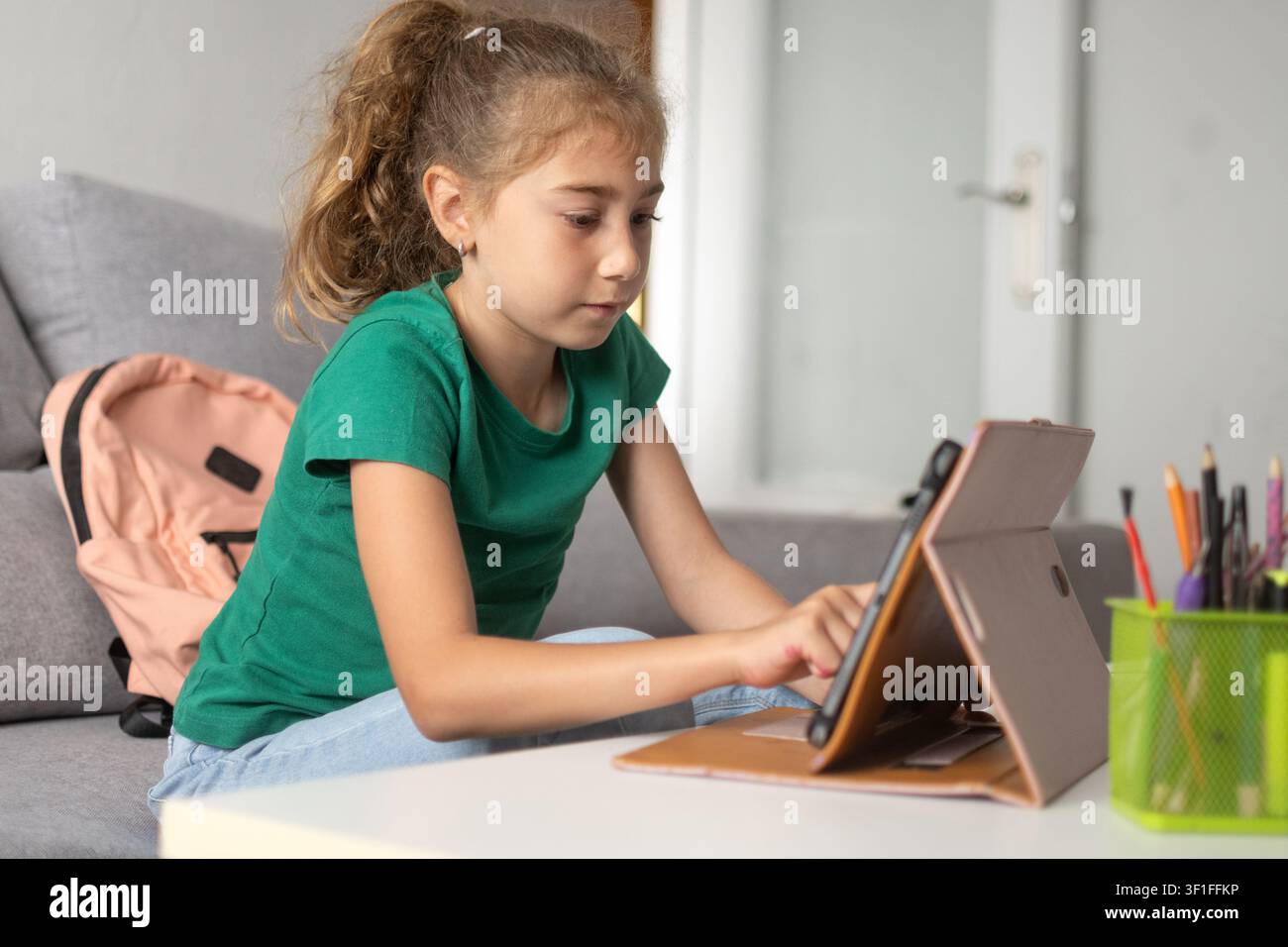 Bambina delle elementari concentrata sul suo tablet mentre studia a casa. Foto Stock