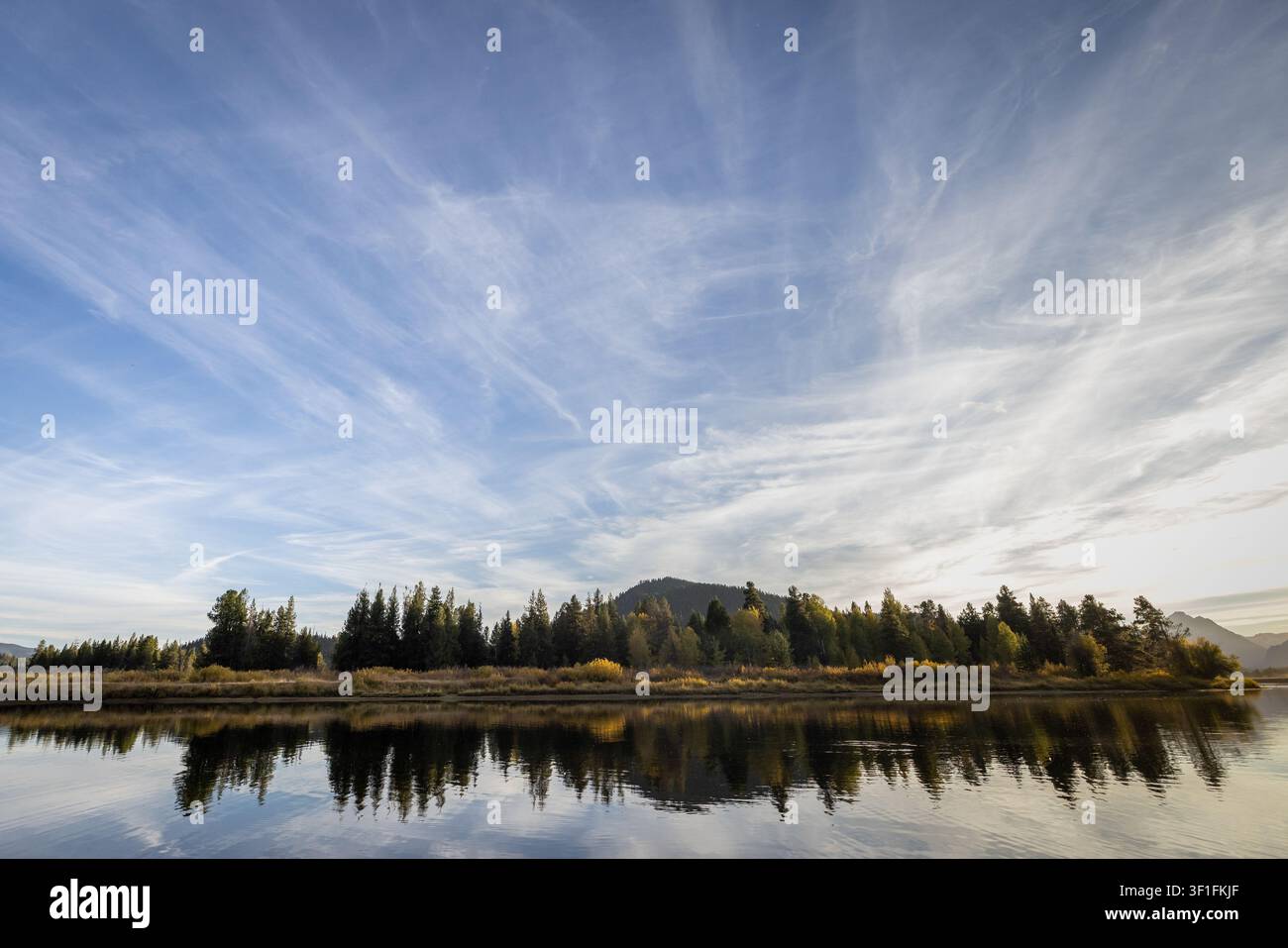 Riva autunnale con riflessi di alberi sotto un cielo azzurro sfumato Foto Stock