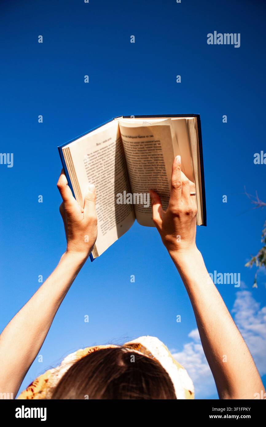 Libro nelle mani di una donna contro il cielo azzurro ad angolo basso. Immagine luminosa per librerie, articoli Foto Stock