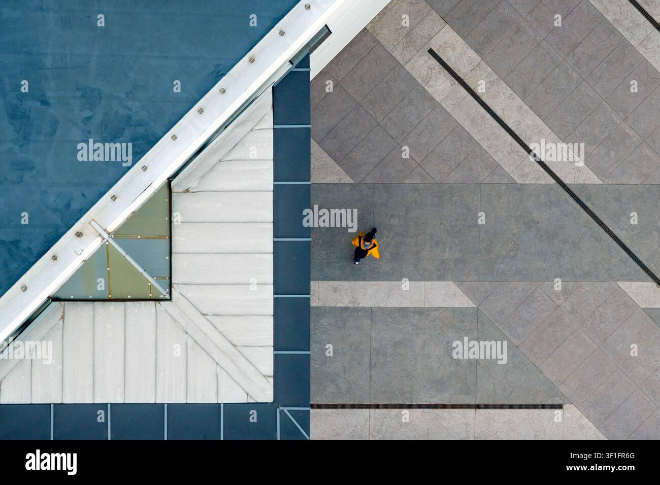 Vista aerea di una persona con giacca gialla che cammina su una piazza geometricamente lastricata accanto a un tetto di edificio moderno a Belgrado, Città di Belgrado, Serbia Foto Stock