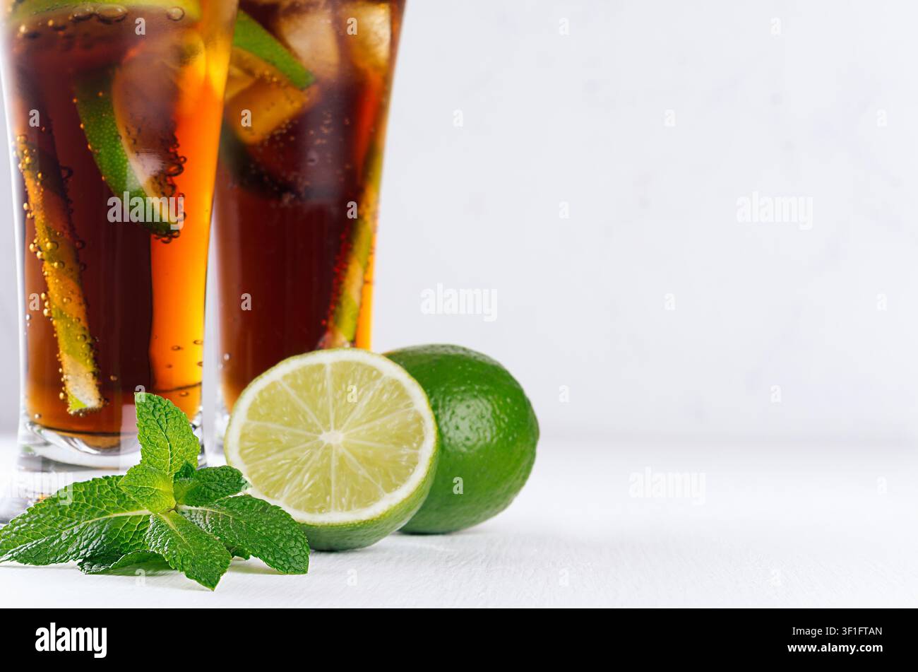 Cocktail freddo cuba libre in due lunghi bicchieri con paglia, pezzi di lime su morbido sfondo bianco moderno, primo piano, consistenza. Foto Stock