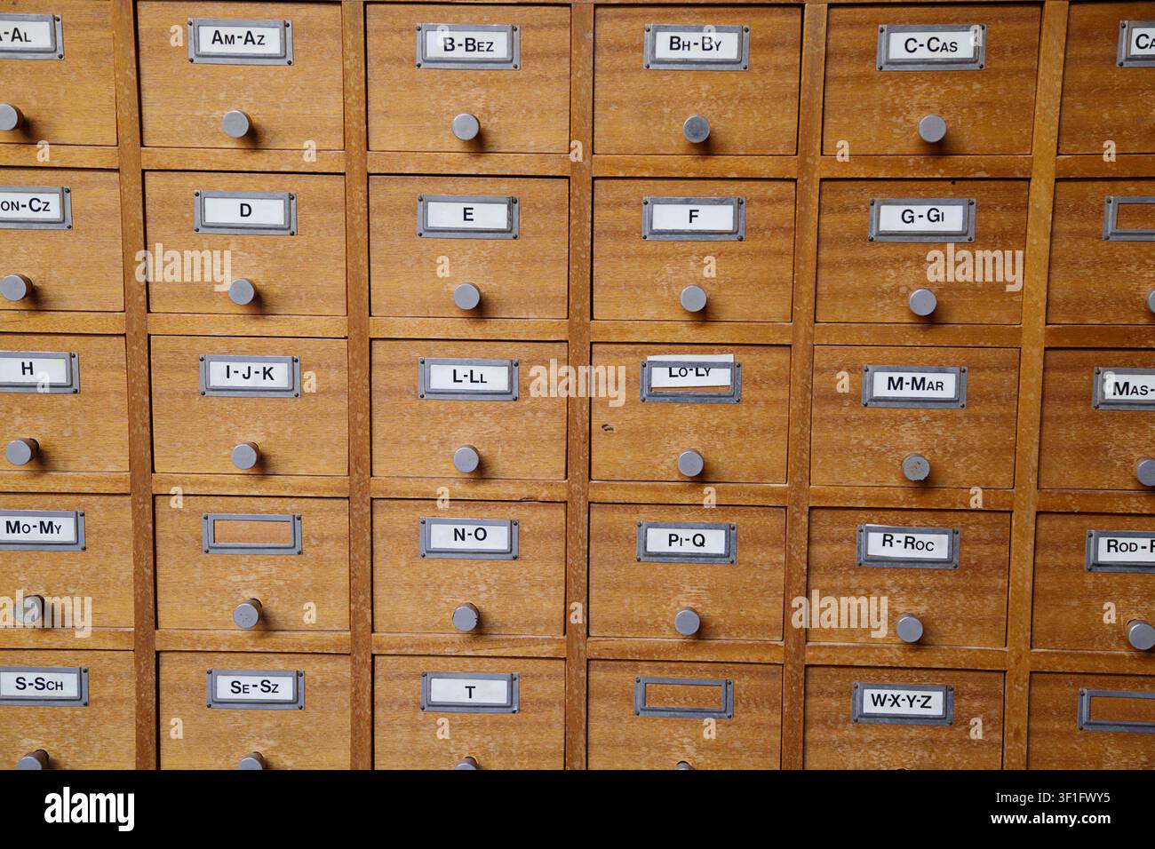 Vista ravvicinata di un armadio di cataloghi cartacei in legno antico con più piccoli cassetti etichettati con schede di indice alfabetico per l'archiviazione vintage in biblioteca Foto Stock