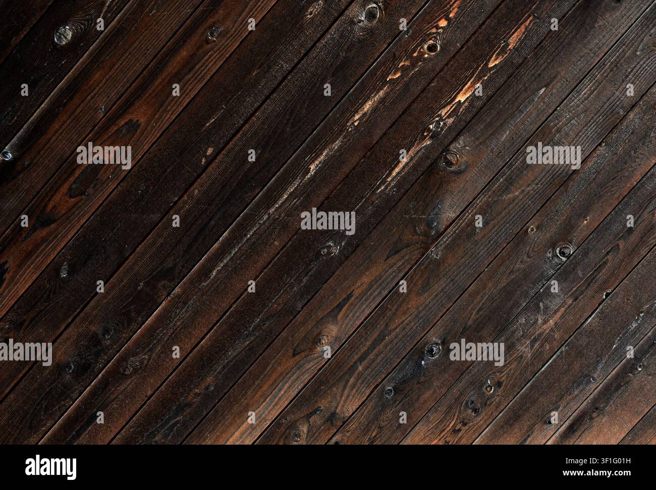 Rivestimento laterale in pannelli di legno macchiati di marrone in diagonale che mostra forti segni di intemperie e una venatura marcata Foto Stock