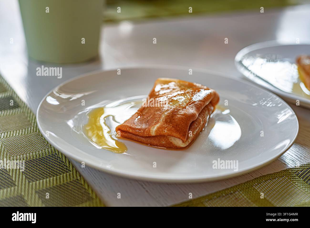 Una pancake ripiegata con miele dolce versato si trova su un piatto di ceramica. Foto Stock