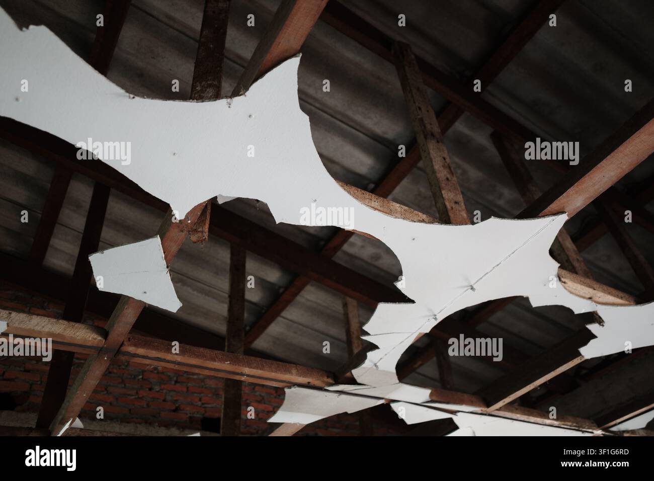 Una prospettiva interna di una stanza in un edificio in ristrutturazione, con un soffitto danneggiato e parzialmente distrutto che rivela le travi del tetto in legno Foto Stock