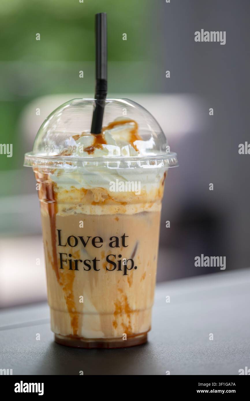 Scatto verticale all'altezza degli occhi di un caffè freddo con panna e gocce di caramello su uno sfondo sfocato all'aperto Foto Stock
