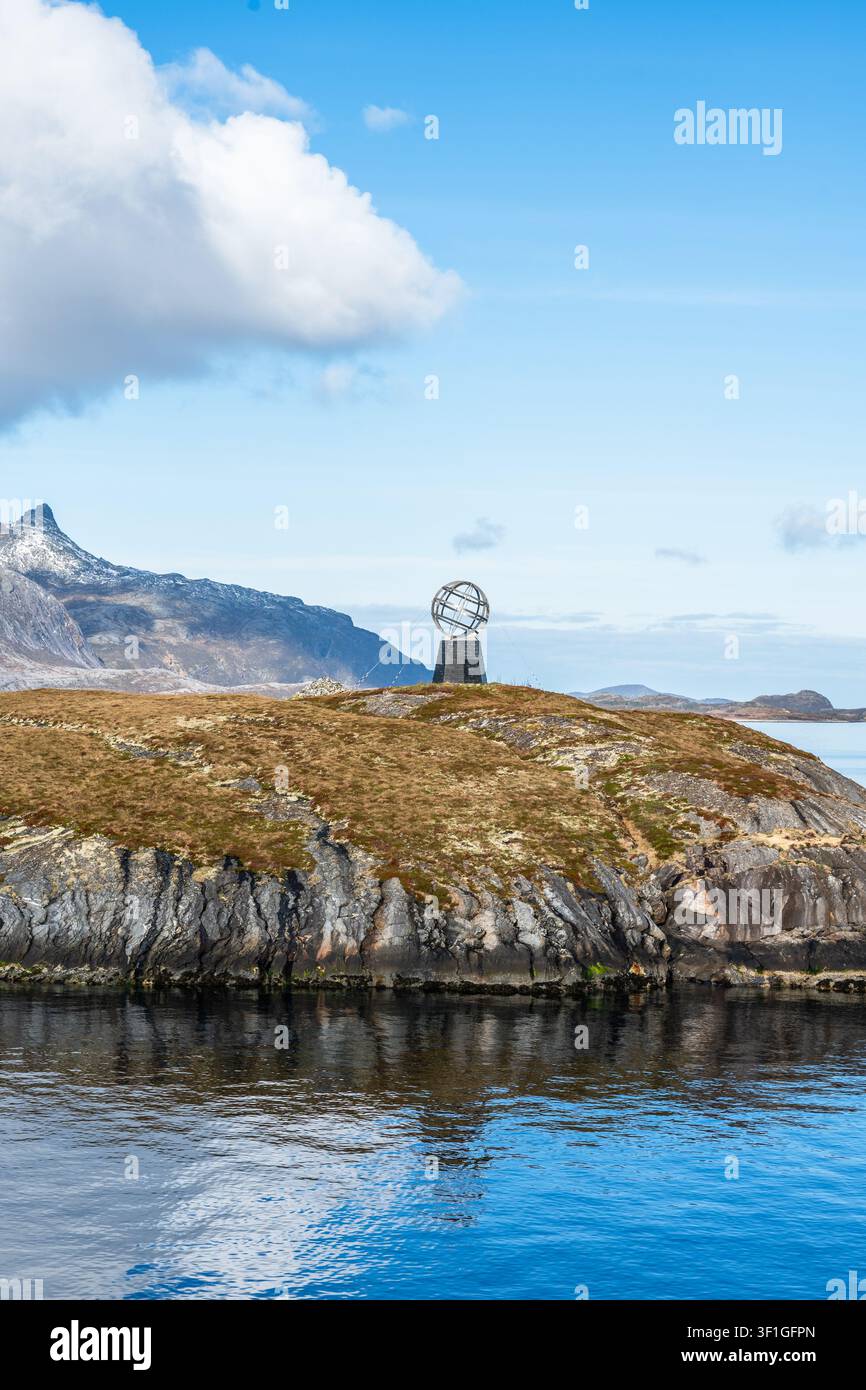 Un monumento si erge sull'isola di Hestmannoy in Norvegia, a segnare il Circolo Polare Artico. Il mare riflette il cielo, e altre isole appaiono in lontananza. Nuvola Foto Stock