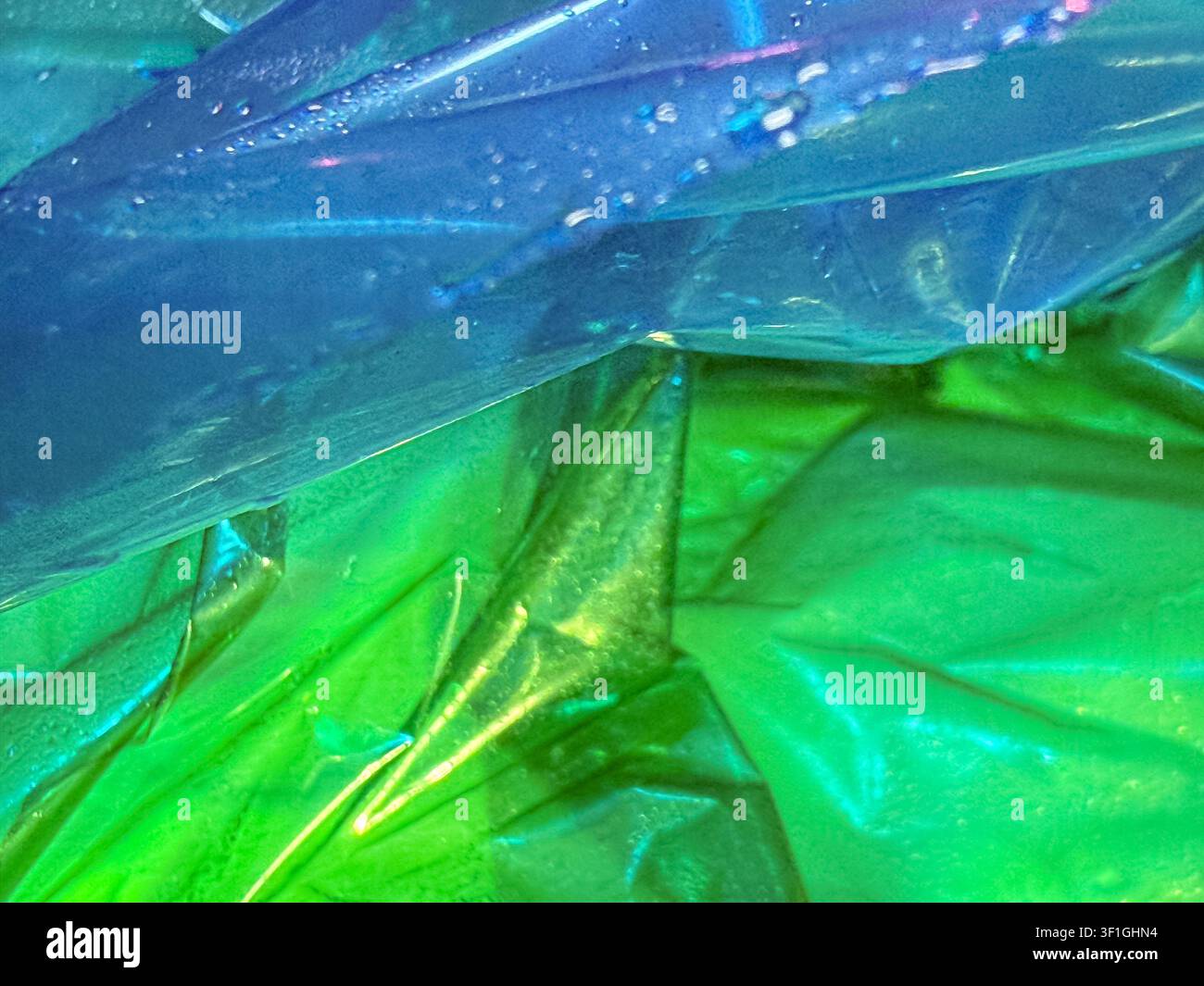 Texture astratta vibrante con strati di cellophane iridescente increspata in blu brillante e verde vivace. Piccole gocce d'acqua aggiungono una trama sottile. Reflec Foto Stock