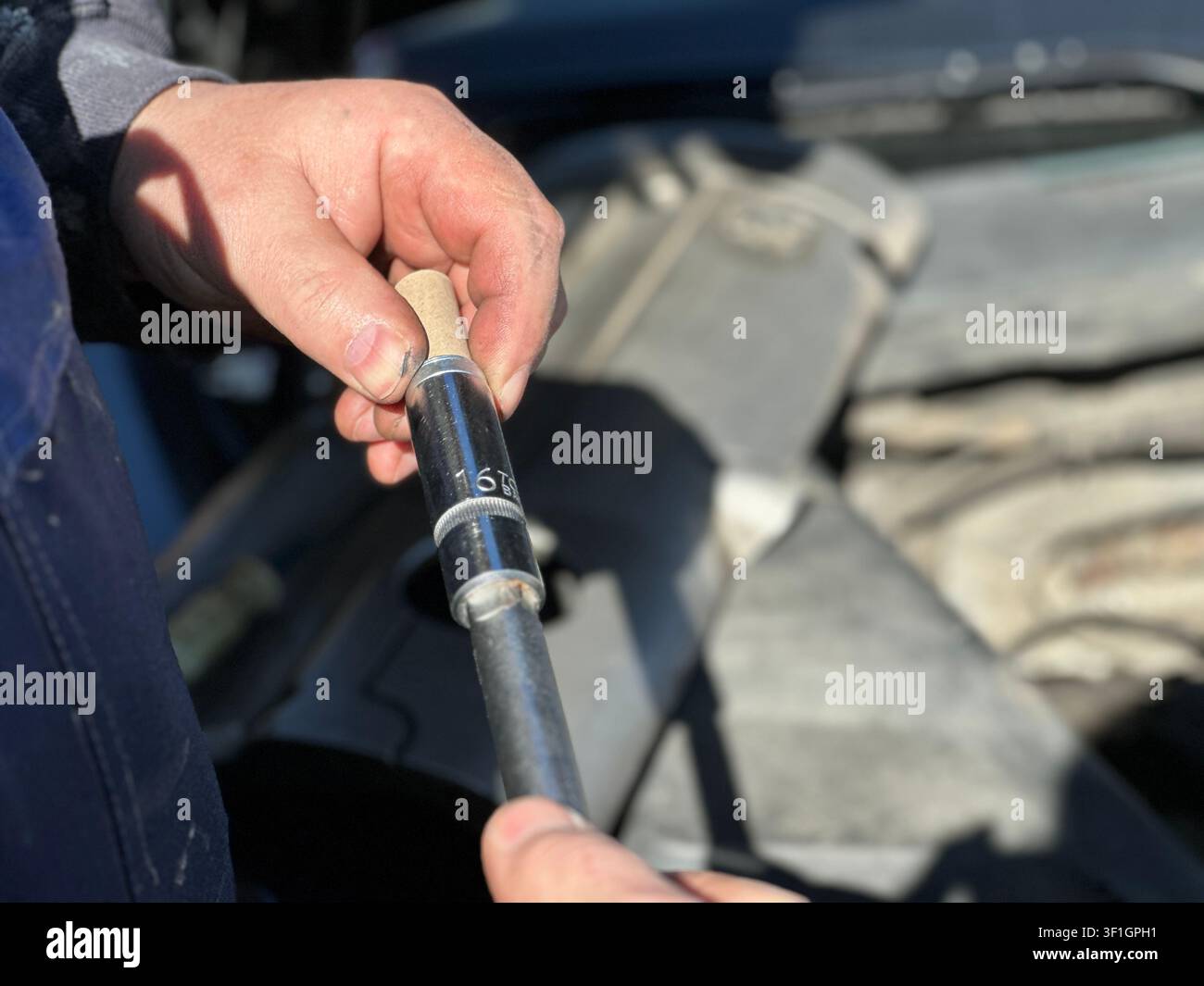 Mani di un meccanico che tengono una nuova candela sopra il vano motore di un'auto - Immagine stock catturata con smartphone