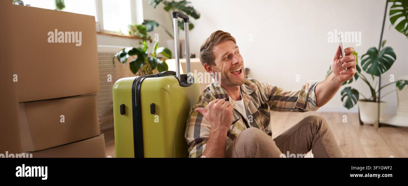 Uomo allegro e sorridente con valigia, videochat con smartphone, selfie e vacanze. Foto Stock