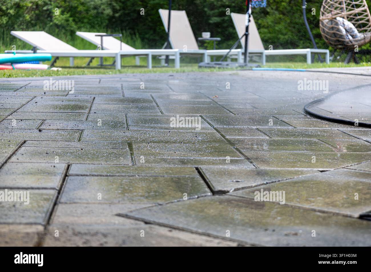 Patio della piscina pulito con pavimentini bagnati interlock durante il restauro prima della risabbiatura in un cortile residenziale. Foto Stock
