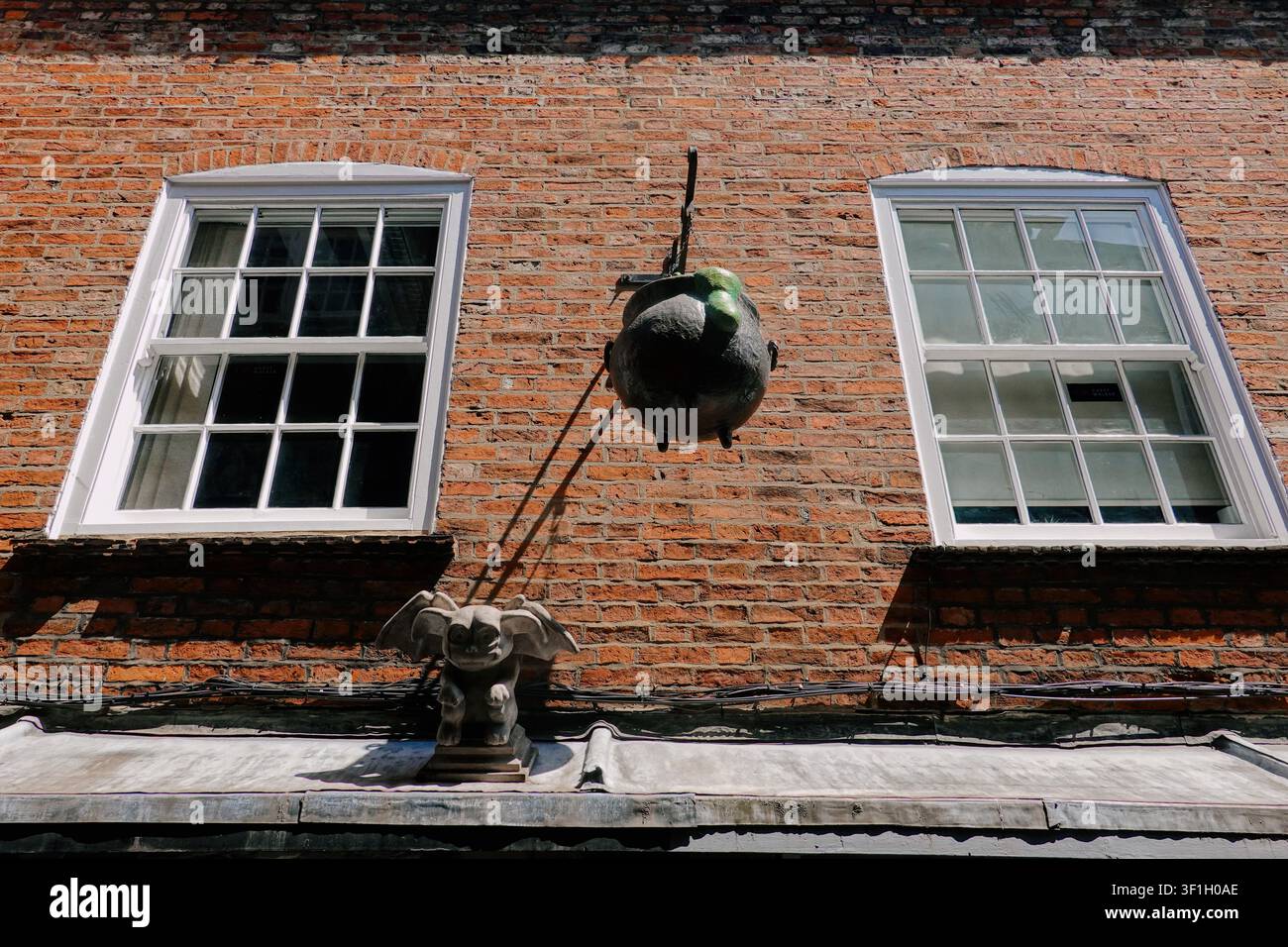 Un cartello a forma di calderone delle streghe appeso e una figura di gargoyle in pietra su una facciata in mattoni rossi nella storica strada Shambles a York, North Yorkshire, Regno Unito. Foto Stock