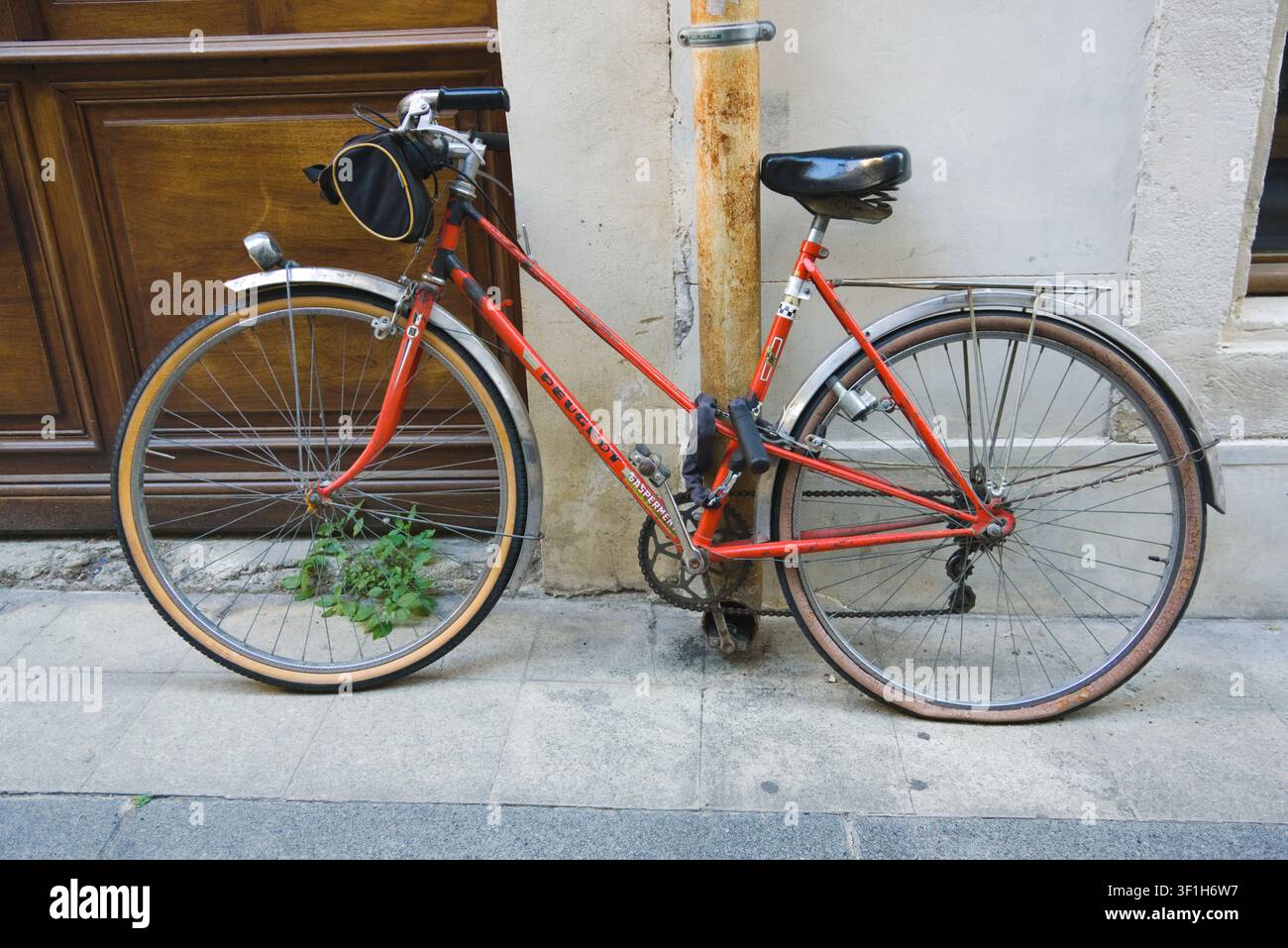 Una classica bicicletta Peugeot rossa con una piccola borsa da sella parcheggiata su una strada accanto a un edificio consumato dal tempo. Arles, Provenza, Francia. Foto Stock